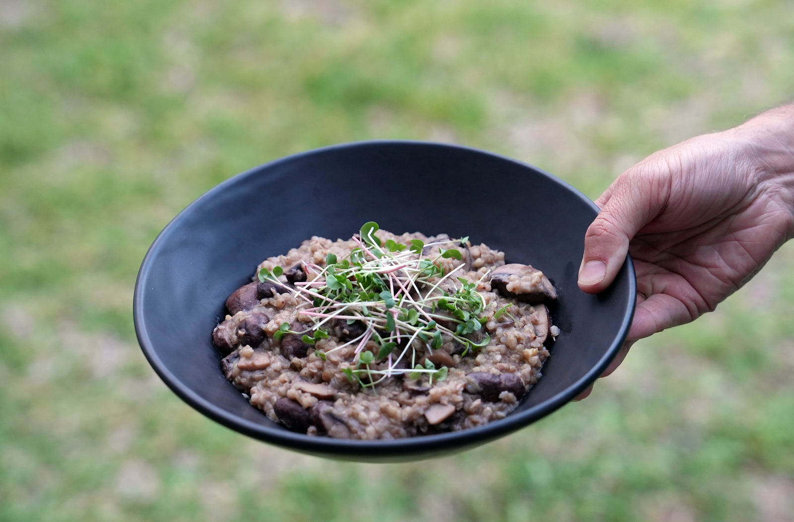 Hand holding bowl of cooked buckwheat groats with mushrooms