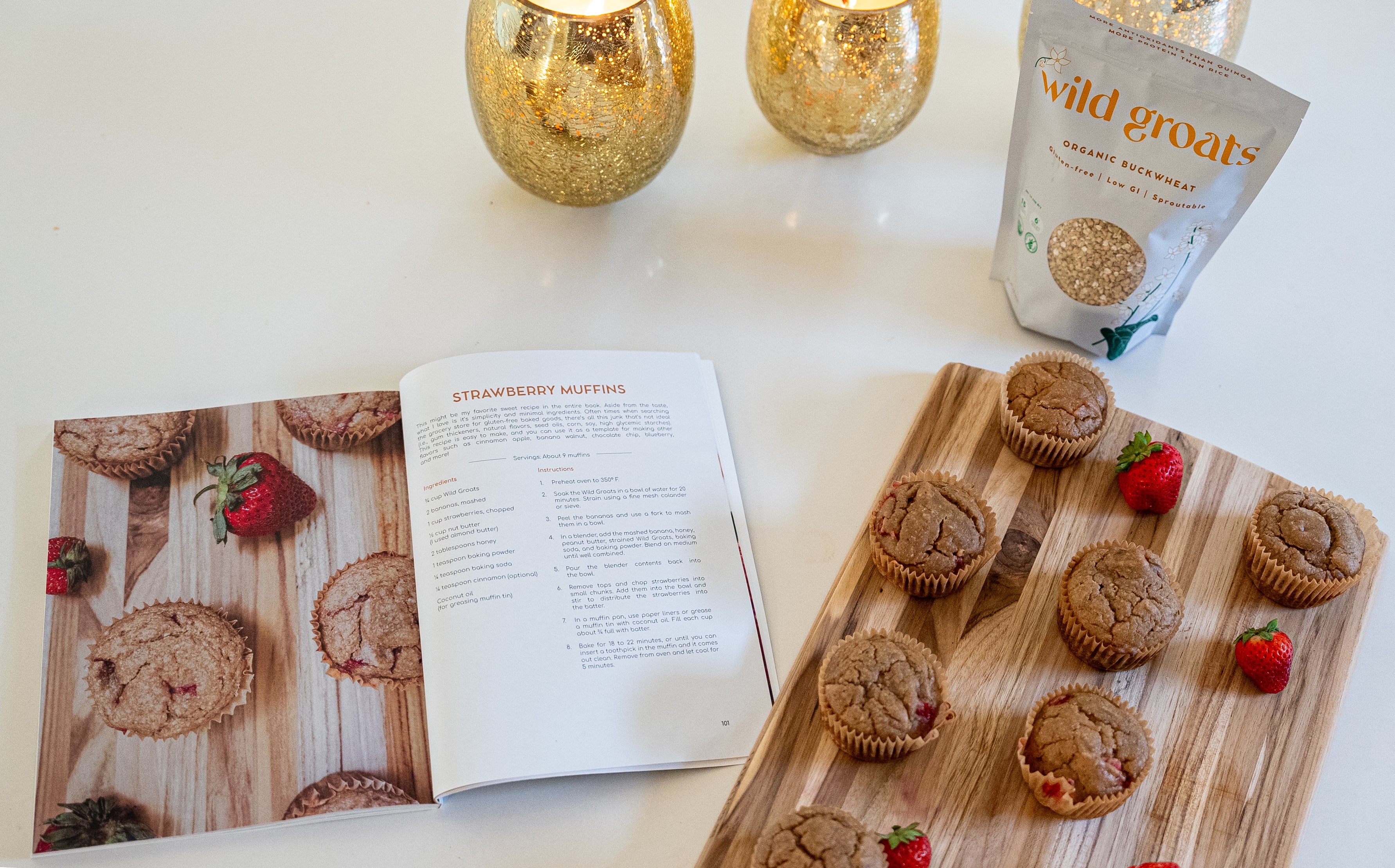 Super Staples recipe book open to strawberry gluten-free muffin page with fresh muffins and Wild Groats bag